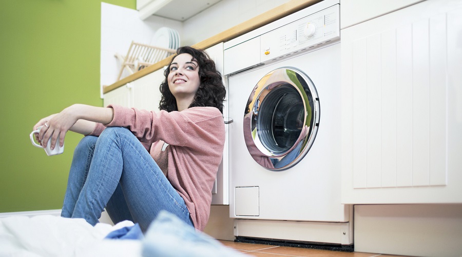 Femme souriante assise devant son lave-linge dans une buanderie verte