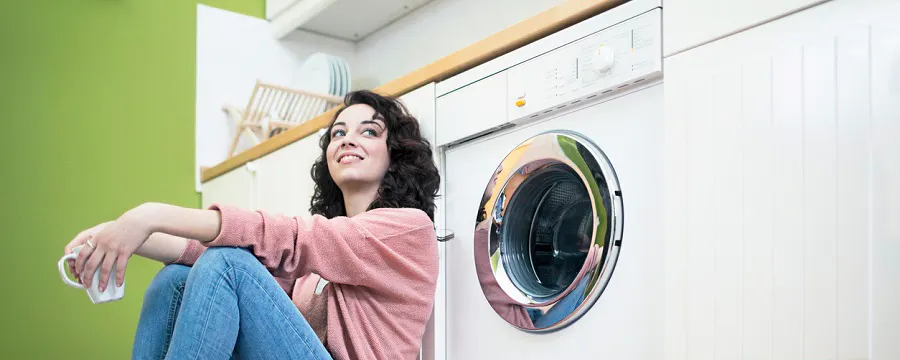Femme souriante assise devant son lave-linge dans une buanderie verte