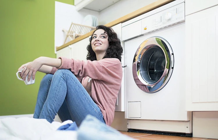 Femme souriante assise devant son lave-linge dans une buanderie verte