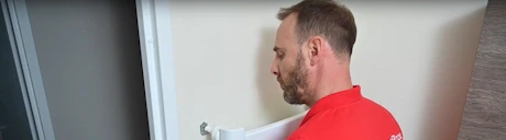 Technicien en polo rouge inspectant une canalisation murale blanche
