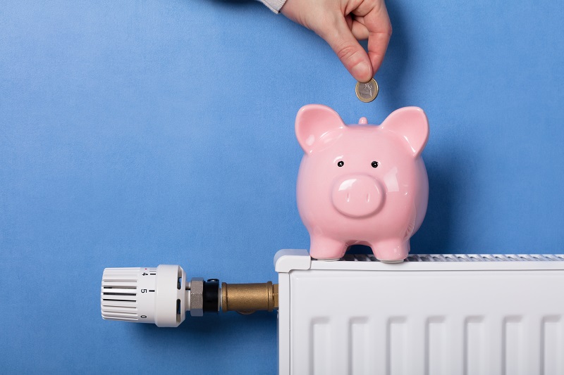 Main déposant une pièce dans une tirelire cochon posée sur un radiateur