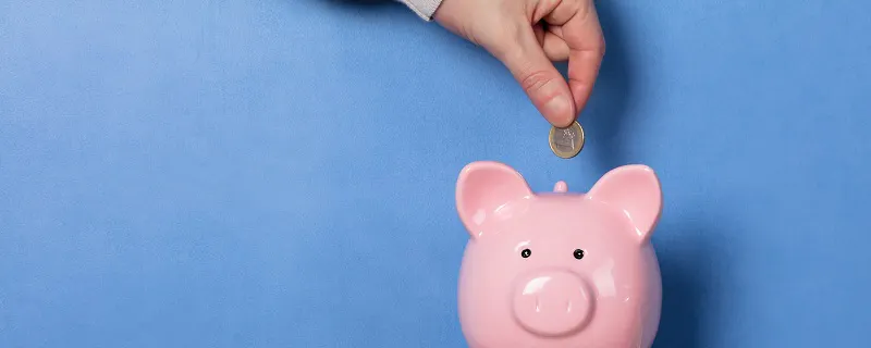 Main déposant une pièce dans une tirelire cochon posée sur un radiateur