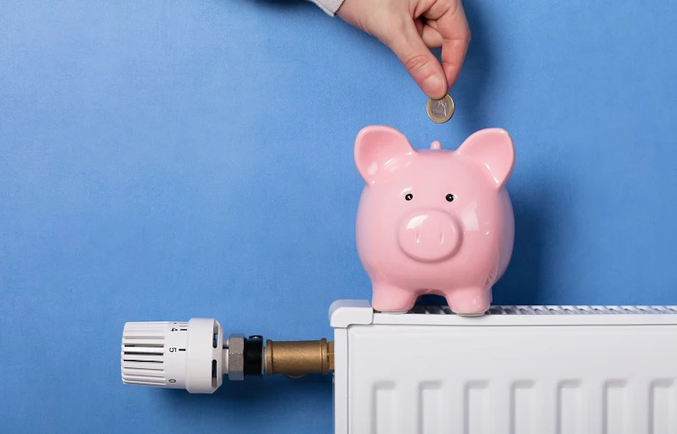 Main déposant une pièce dans une tirelire cochon posée sur un radiateur