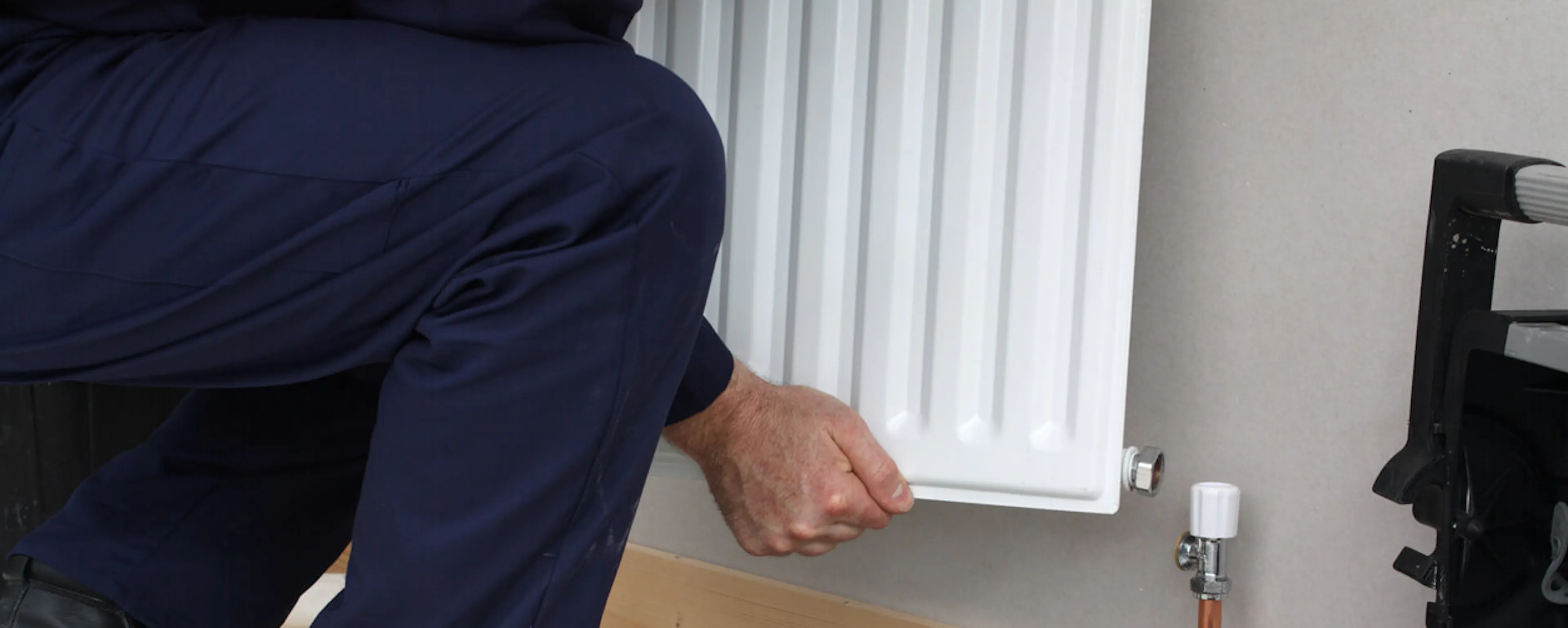 Plombier en combinaison bleue travaillant près d'un radiateur avec des outils