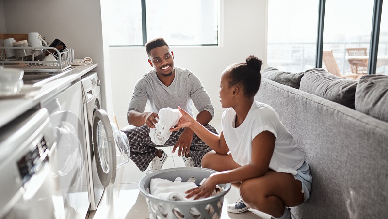 Couple souriant faisant la lessive ensemble devant un lave-linge