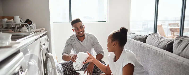 Couple souriant faisant la lessive ensemble devant un lave-linge