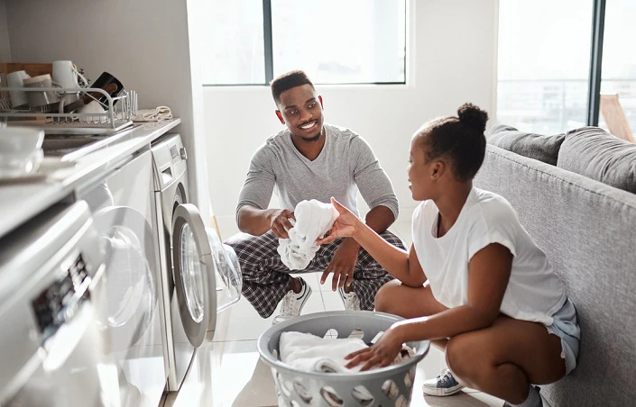 Couple souriant faisant la lessive ensemble devant un lave-linge