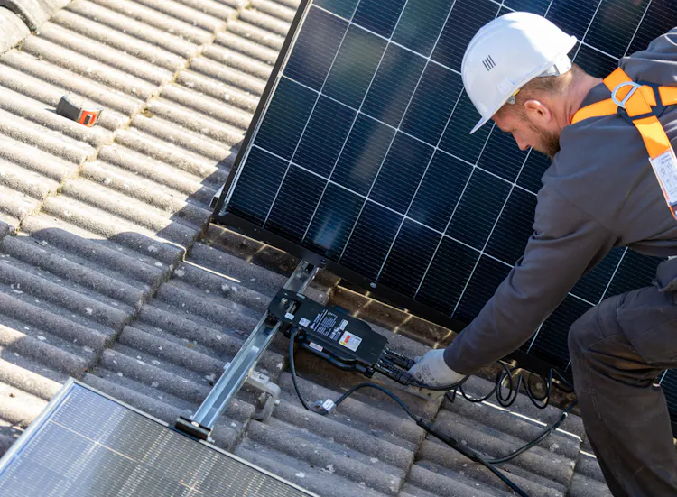 Technicien en toiture câblant un micro-onduleur lors de l'installation de panneaux solaires photovoltaïques