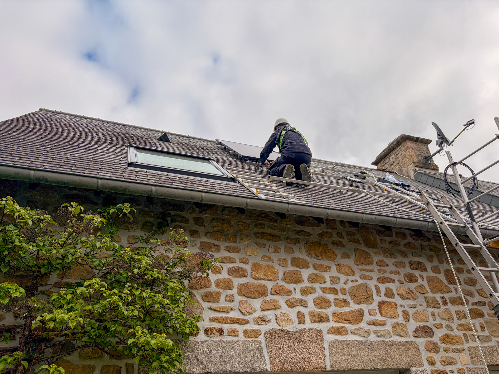 Technicien VIK Energies, sur le toit d'une maison en pierre normande, en train d'installer des panneaux solaires