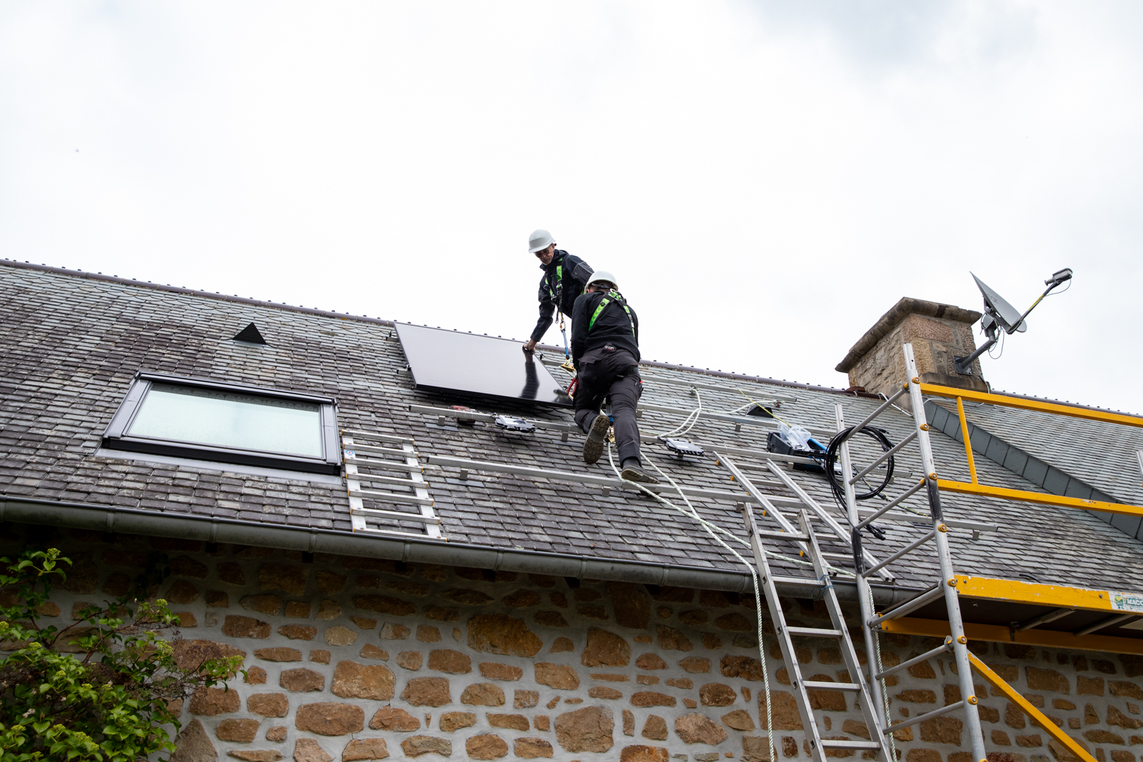 Deux techniciens VIK Energies en train d'installer des panneaux solaires sur le toit d'une maison en pierre près de Quettehou dans la Manche
