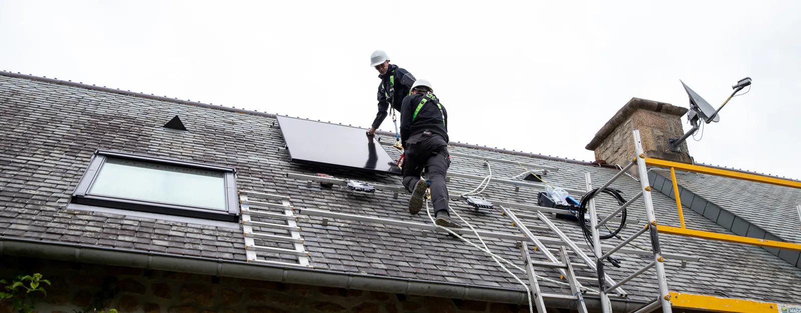 Deux techniciens VIK Energies en train d'installer des panneaux solaires sur le toit d'une maison en pierre près de Caen, après validation du devis