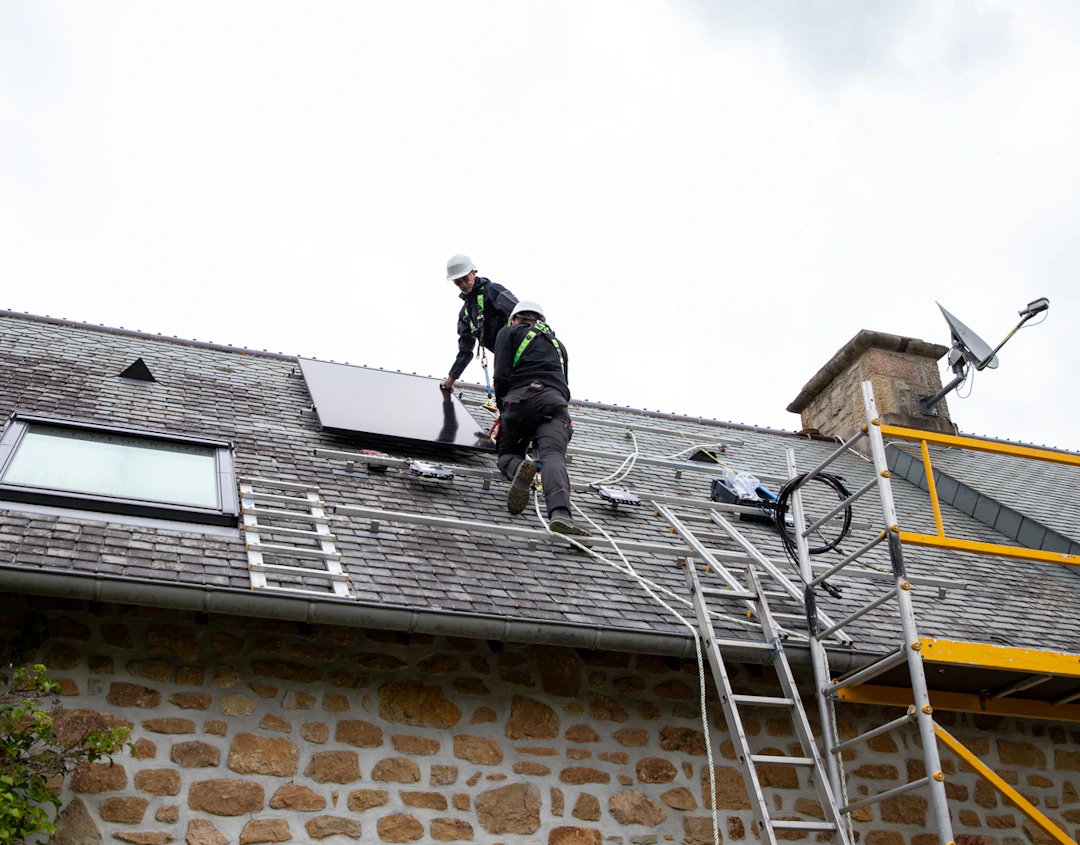 Deux techniciens VIK Energies en train d'installer des panneaux solaires sur le toit d'une maison en pierre près des Pieux dans la Manche