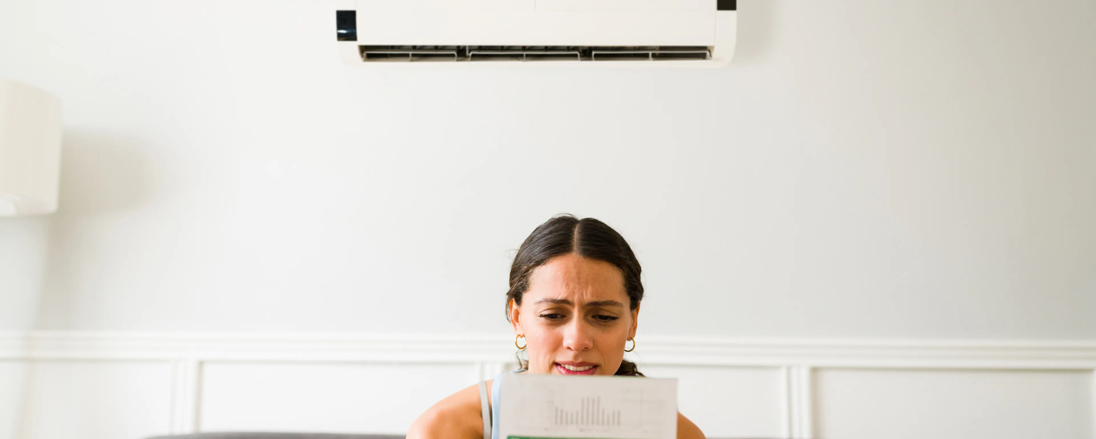 Consommation d’énergie d’une climatisation réversible : une femme regarde sa facture d'électricité devant sa climatisation