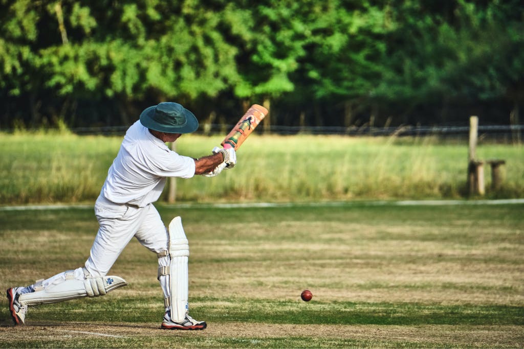 A man in a green hat swings a cricket bat at a ball