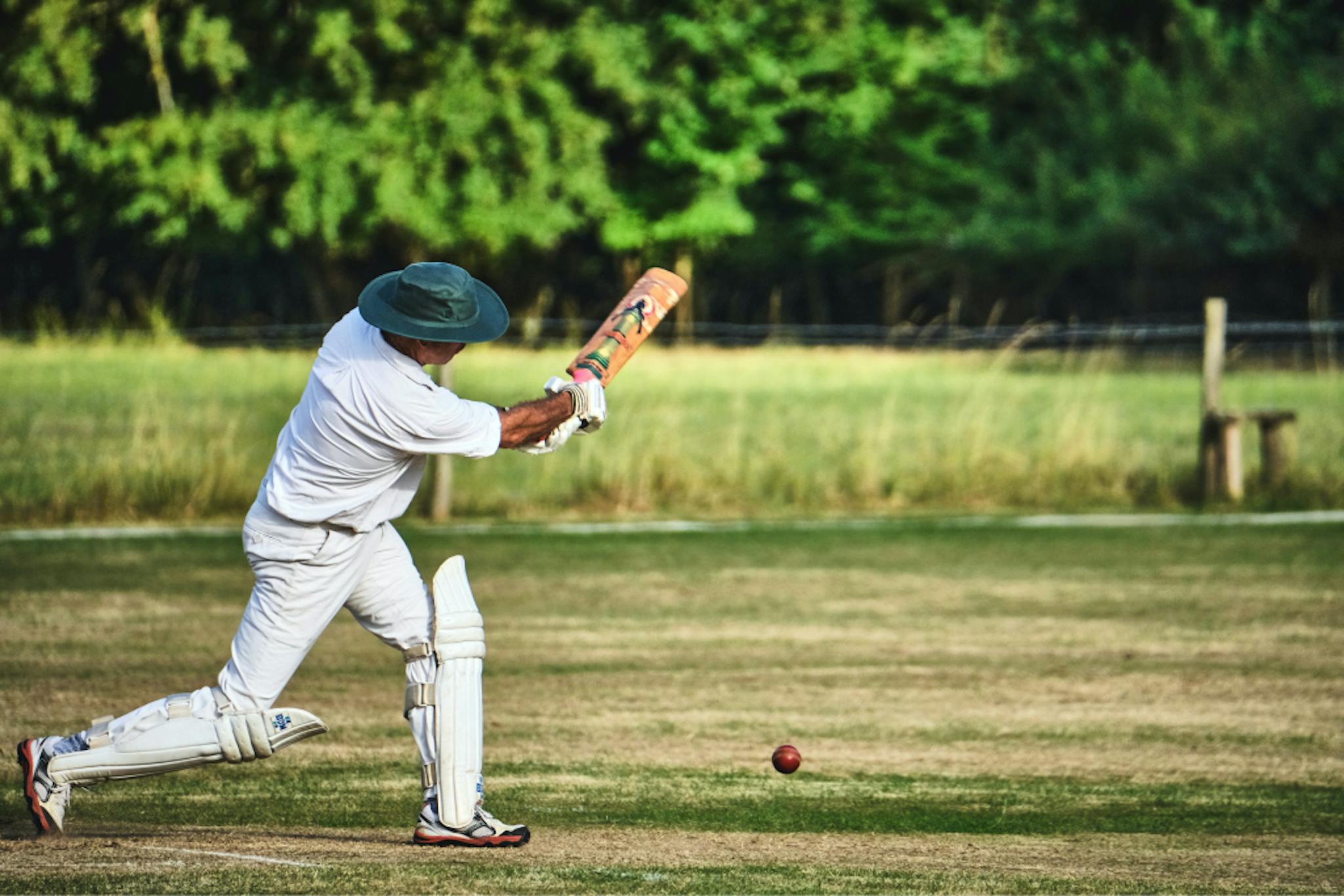 A man in a green hat swings a cricket bat at a ball