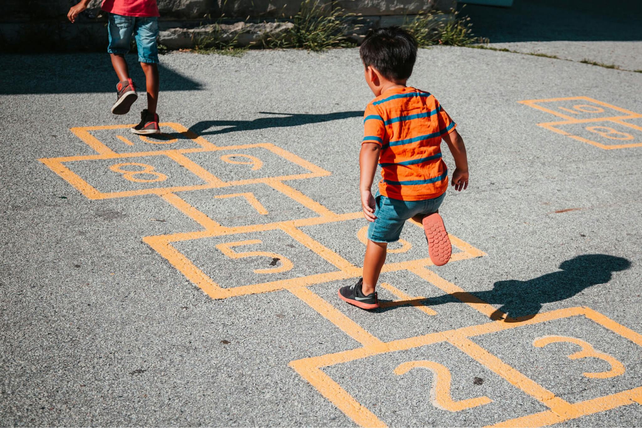 A child in an orange and green striped shirt plays hopscotch