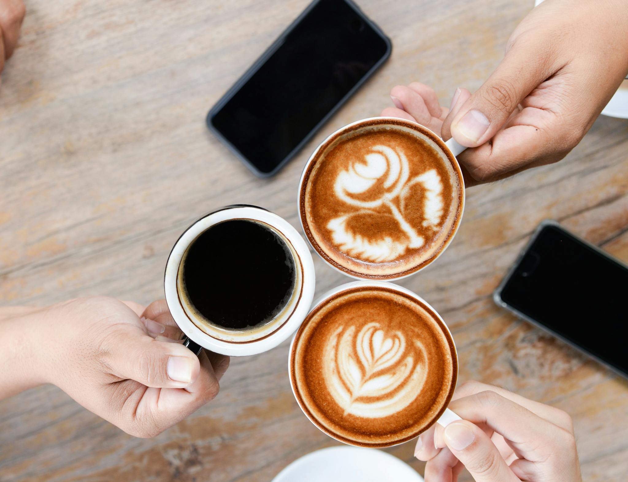 Two lattes and a black coffee, with two photos sitting on a wooden table in the background