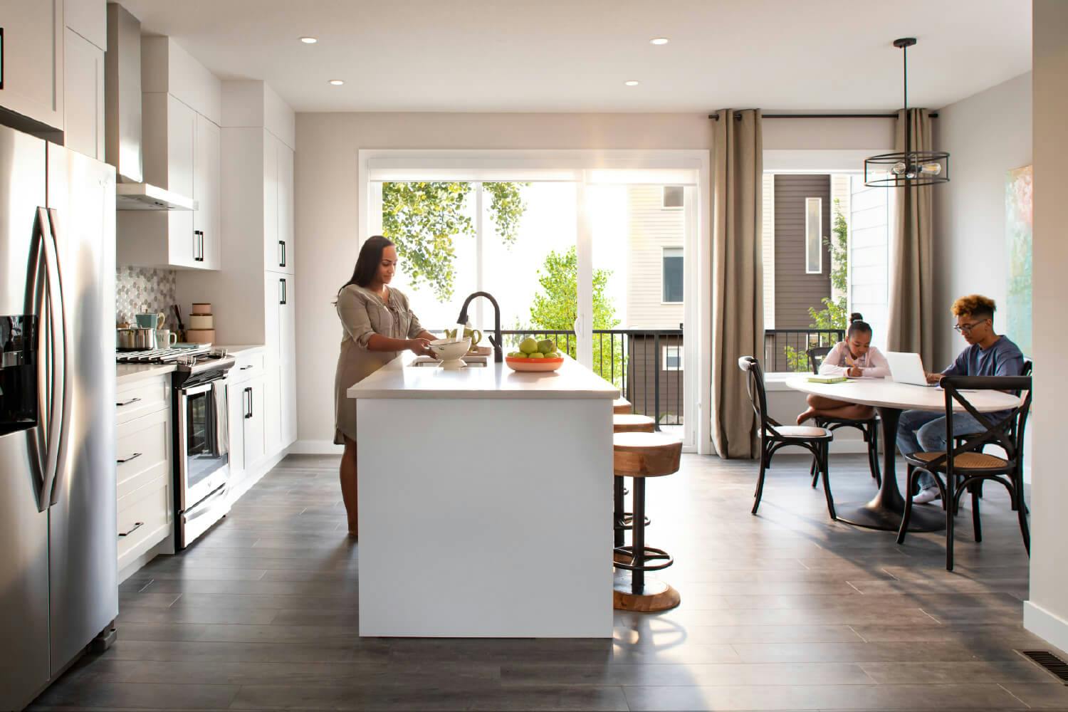 White and brown kitchen with a mother and two children working on their respective projects.