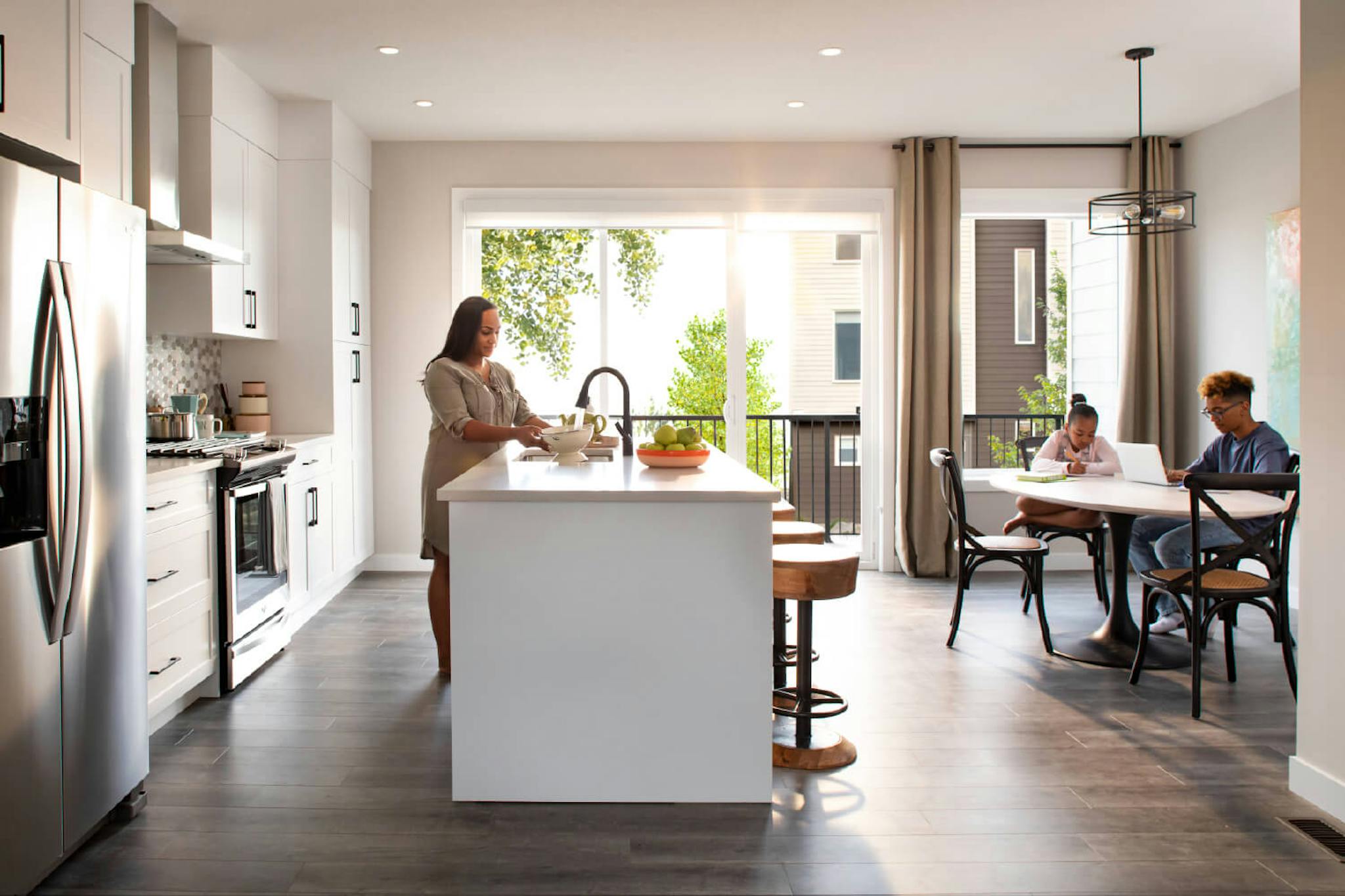 White and brown kitchen with a mother and two children working on their respective projects.