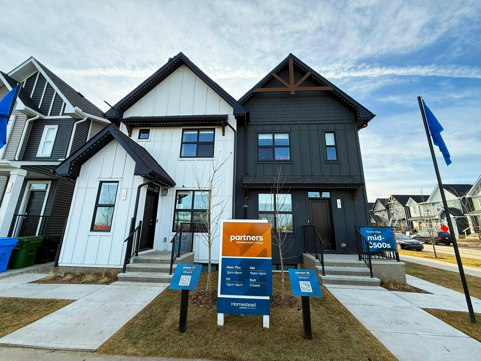 Light and dark duplexes by Partners Homes, side by side under a blue sky.