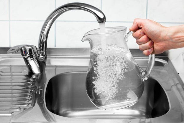 Man Holds Clear Pitcher of Water as Faucet Fills Up