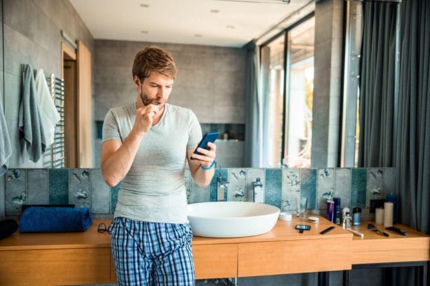 Man Brushing Teeth While Holding Phone