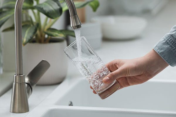 Hard Water Problems Hand Holds Glass as it Pours Out of Faucet