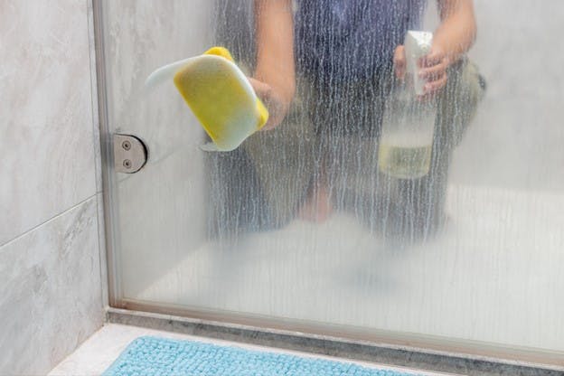 Woman Washes Shower Door Frim Calcium Buildup
