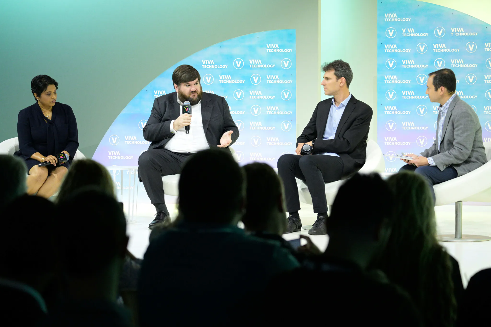 Dr Joe Fitzsimons holds a microphone and speaks to three other panelists on stage at VivaTech