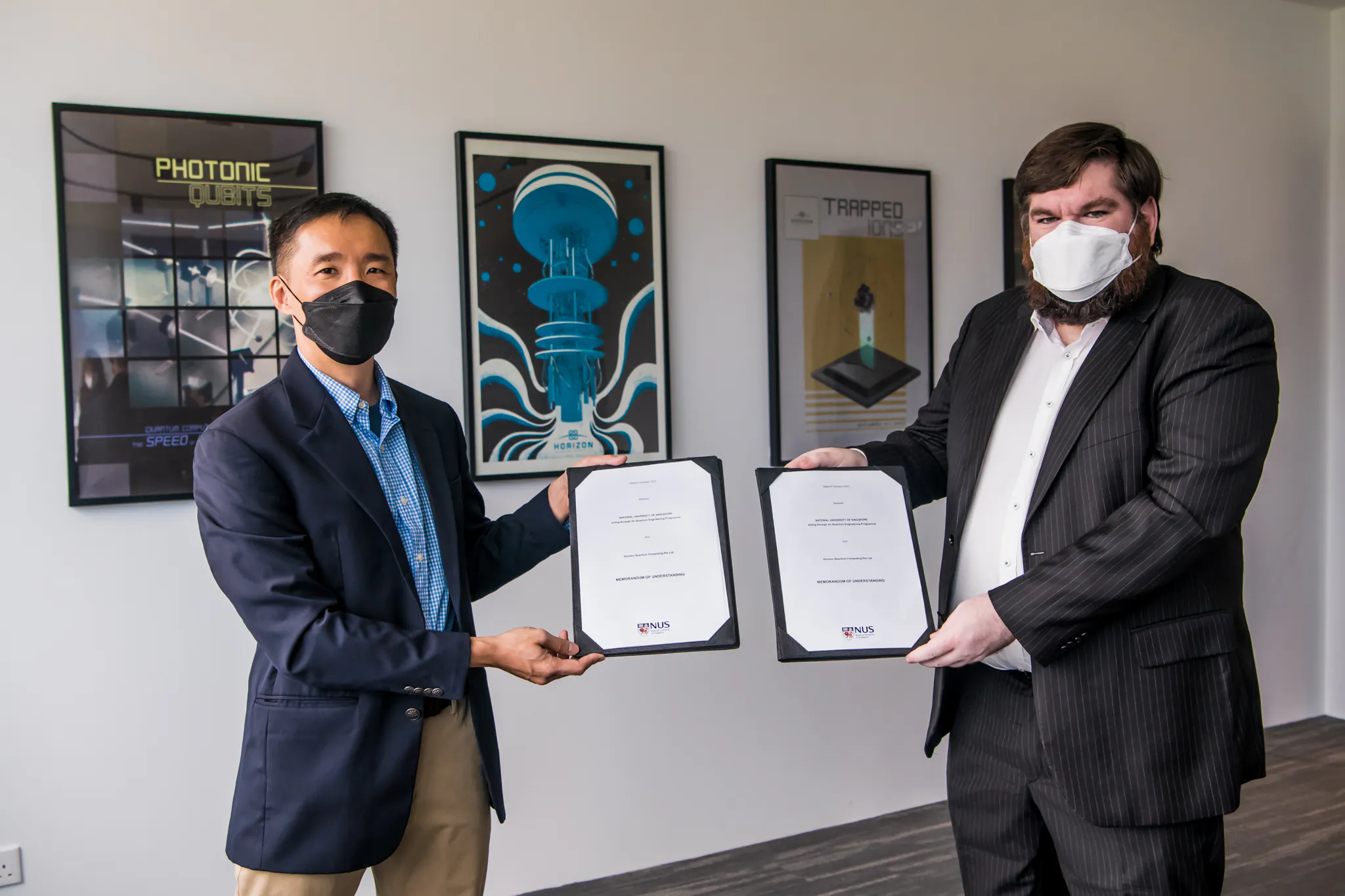 Horizon Quantum CEO Joe Fitzsimons and Alexander Ling holding signed MoUs. They're wearing masks and standing in front of quantum computing posters in Horizon's Singapore office.