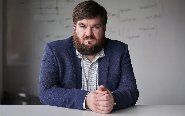 Dr Joe Fitzsimons sitting at a desk with a whiteboard behind him