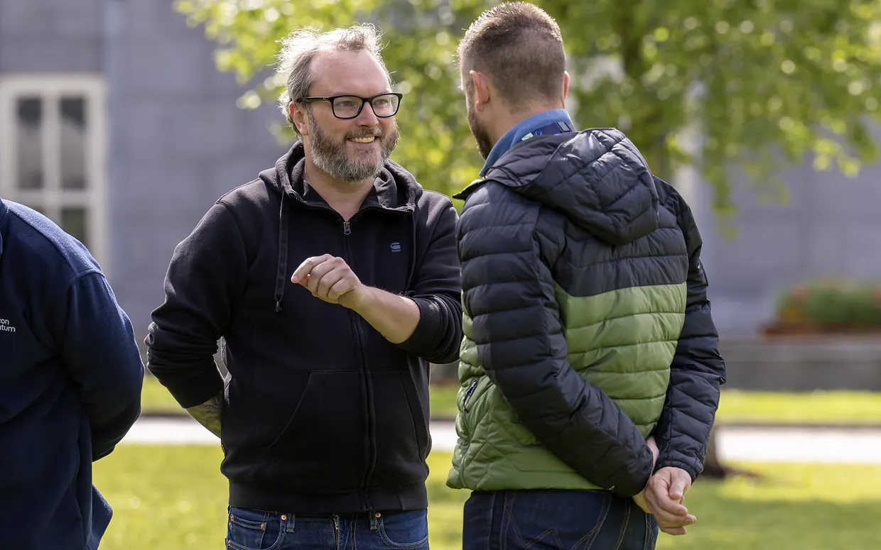 A Horizon team member stands outside at the 2025 offsite. He's smiling and talking with another team member, whose back is to the camera.