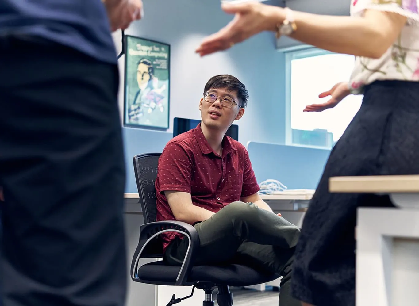 A Horizon team member sits in his chair in the Singapore office, looking up at two people talking. Their faces are off-camera.