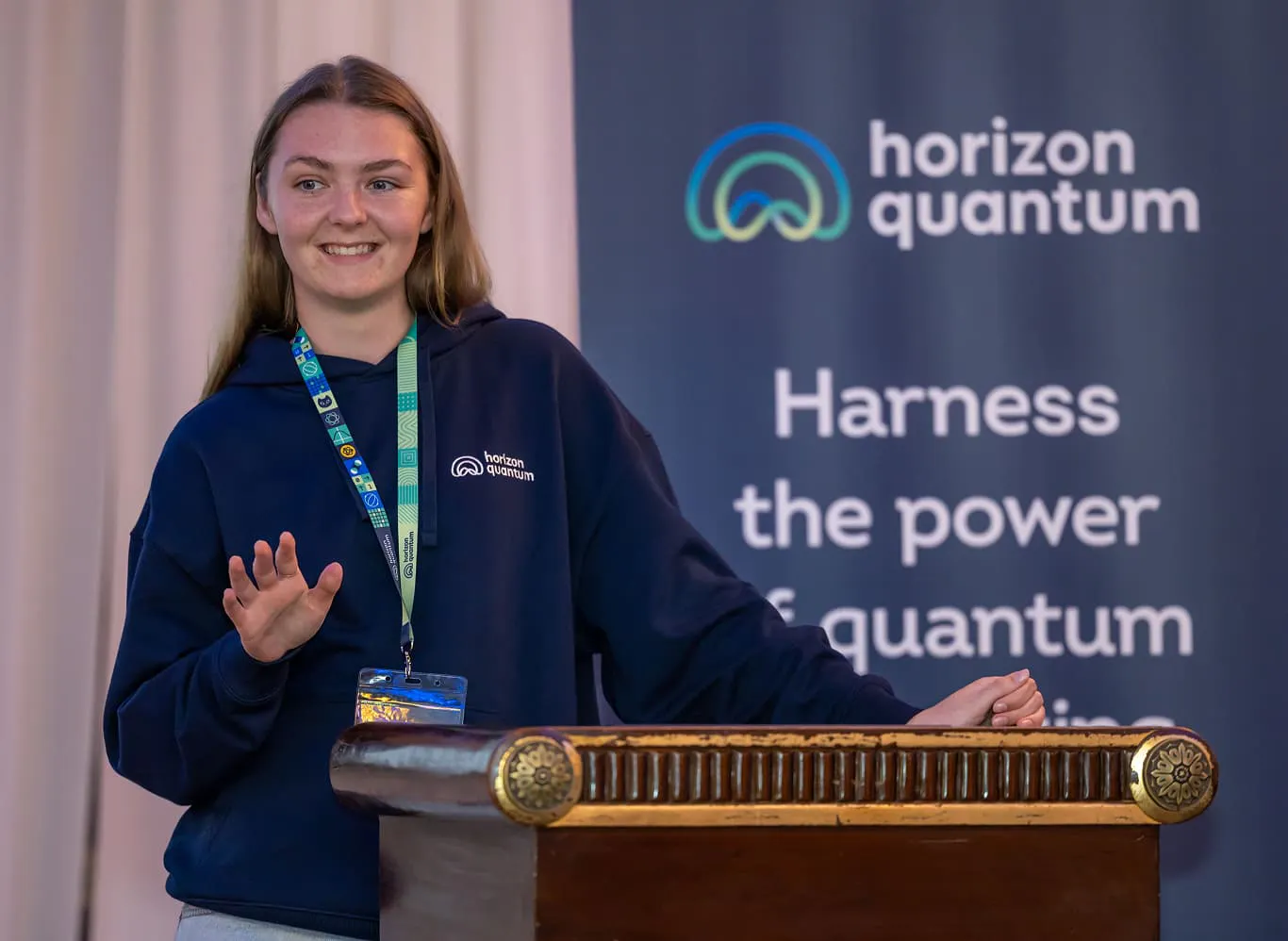 A Horizon team member standing next to a podium with the Horizon Quantum backdrop behind her as she gives a presentation