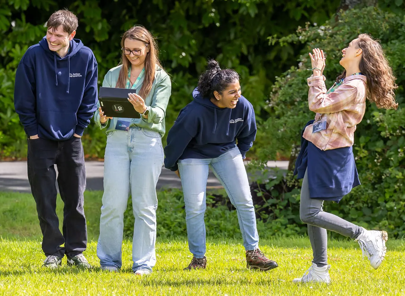 Four Horizon team members outside at the company offsite, participating in a group activity. One holds a table while the other three are laughing. 
