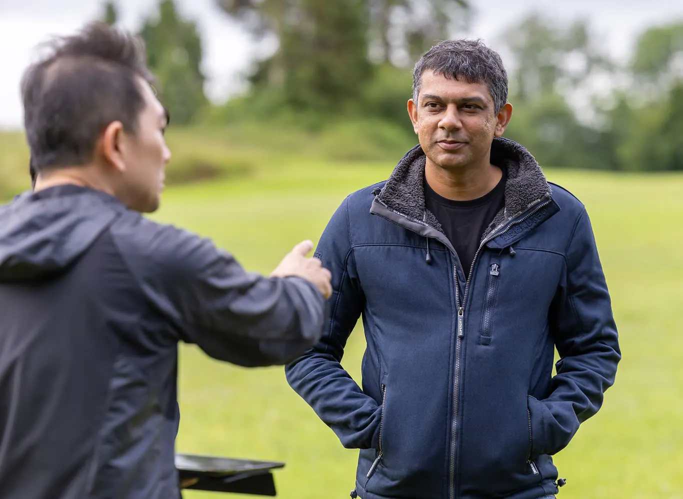 Two Horizon team members speak outside at the company offsite. One has his back towards the camera, but the other looks focused with both hands in his coat pockets.