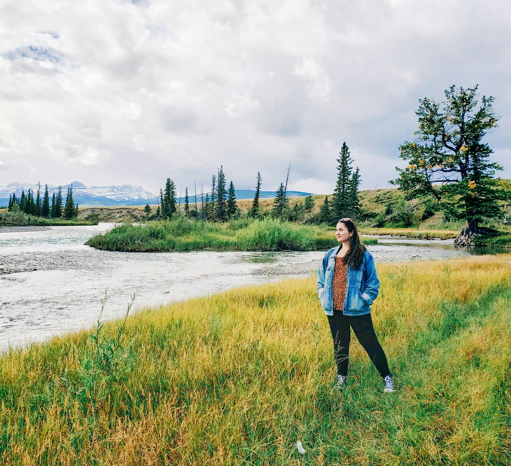 Leah stands at the edge of a river with the Rocky Mountains in the distance.