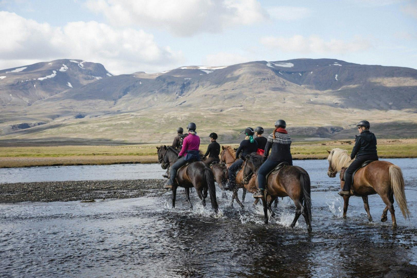 A group of riders cross a river on horseback in a beautiful Icelandic landscape