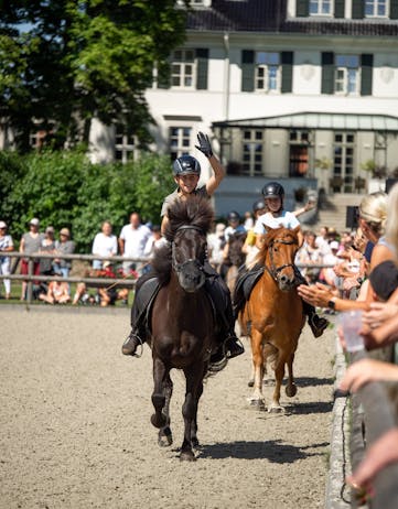 Children ride their Icelandic horses on the arena in front of a crowd of people, clapping.