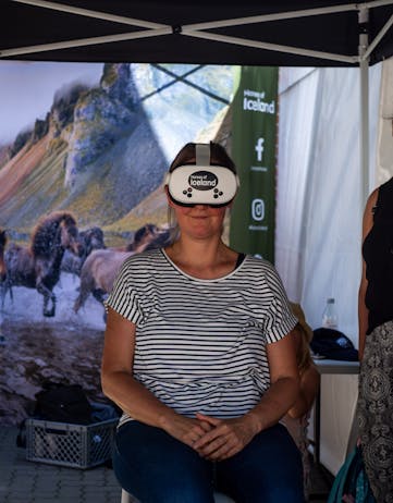 A woman sits and smiles with the Horses of Iceland VR glasses on her head.