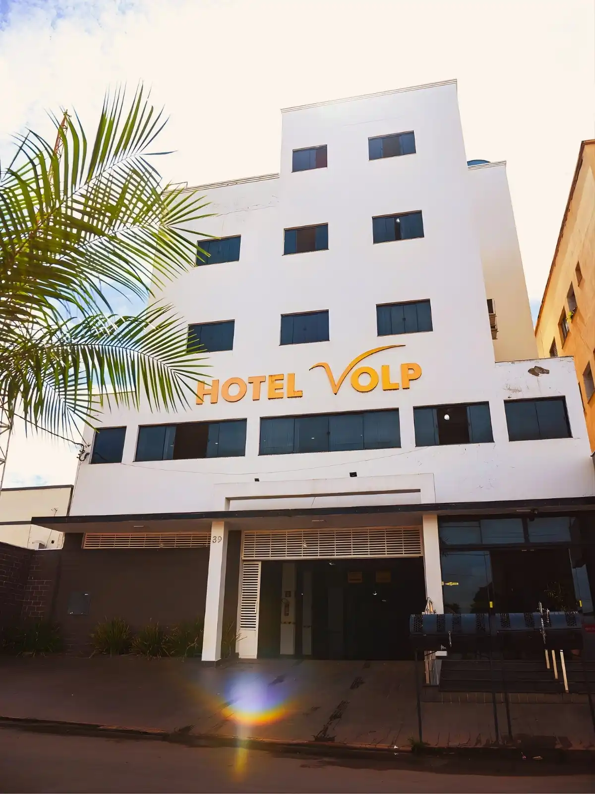 Fachada do Hotel Volp, um hotel moderno e bem localizado na cidade, com fachada branca, janelas escuras e destaque para o nome em amarelo na fachada.