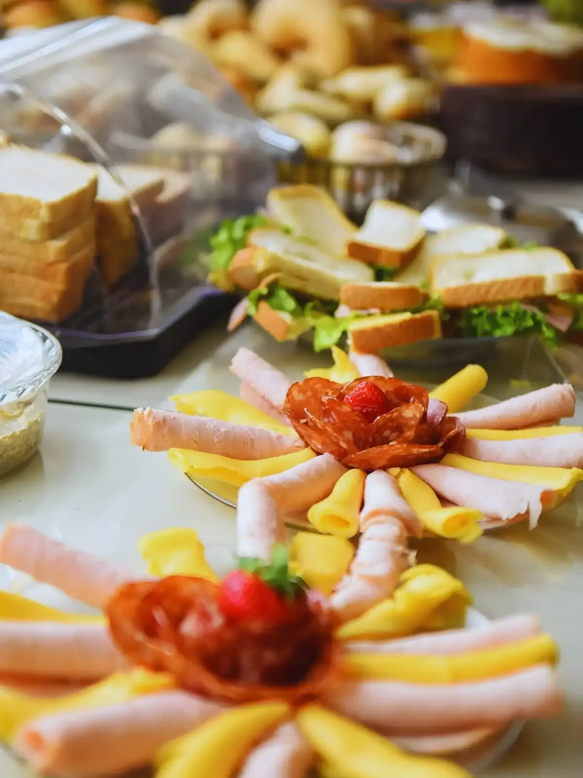 Panela com frios variados, incluindo salame, presunto e queijo, decorada com tomate e pimentão, em uma apresentação para buffet ou festa.