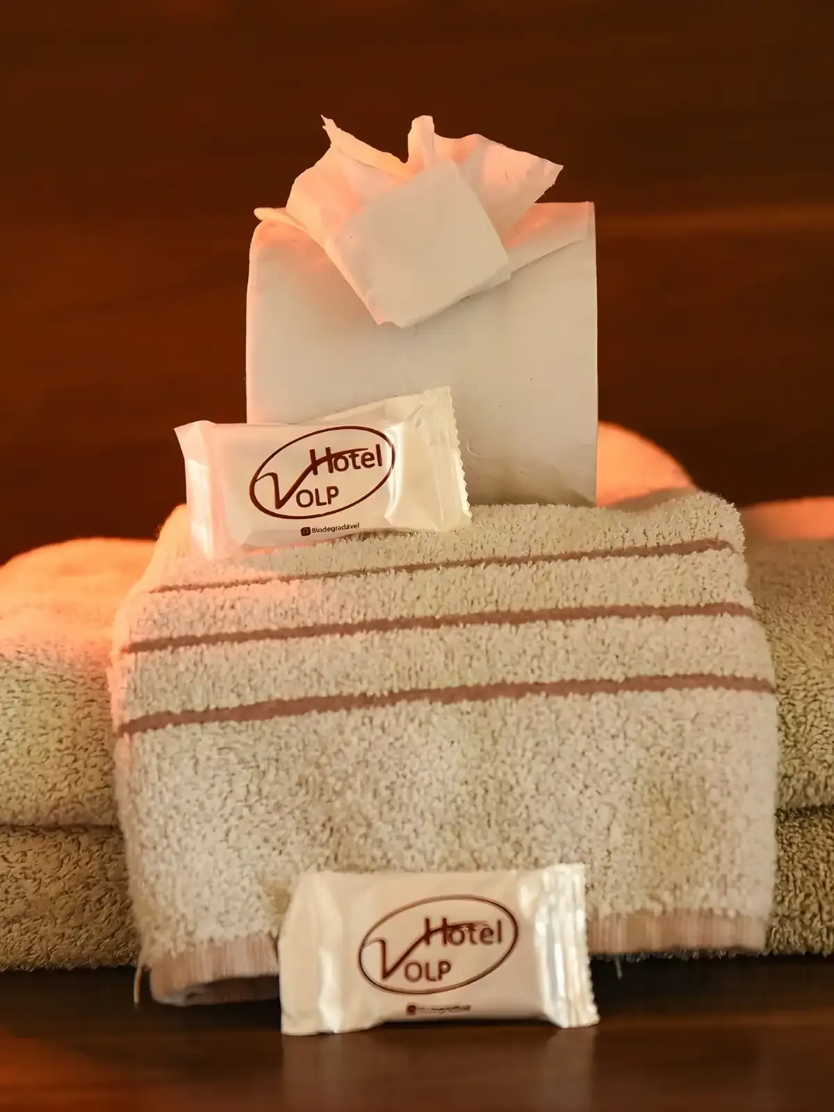 Toalha de banho, sabonetes e papel higiênico com logo do Hotel VLP, itens de hotelaria sobre toalha. Organização de amenities de hotel com foco em conforto.