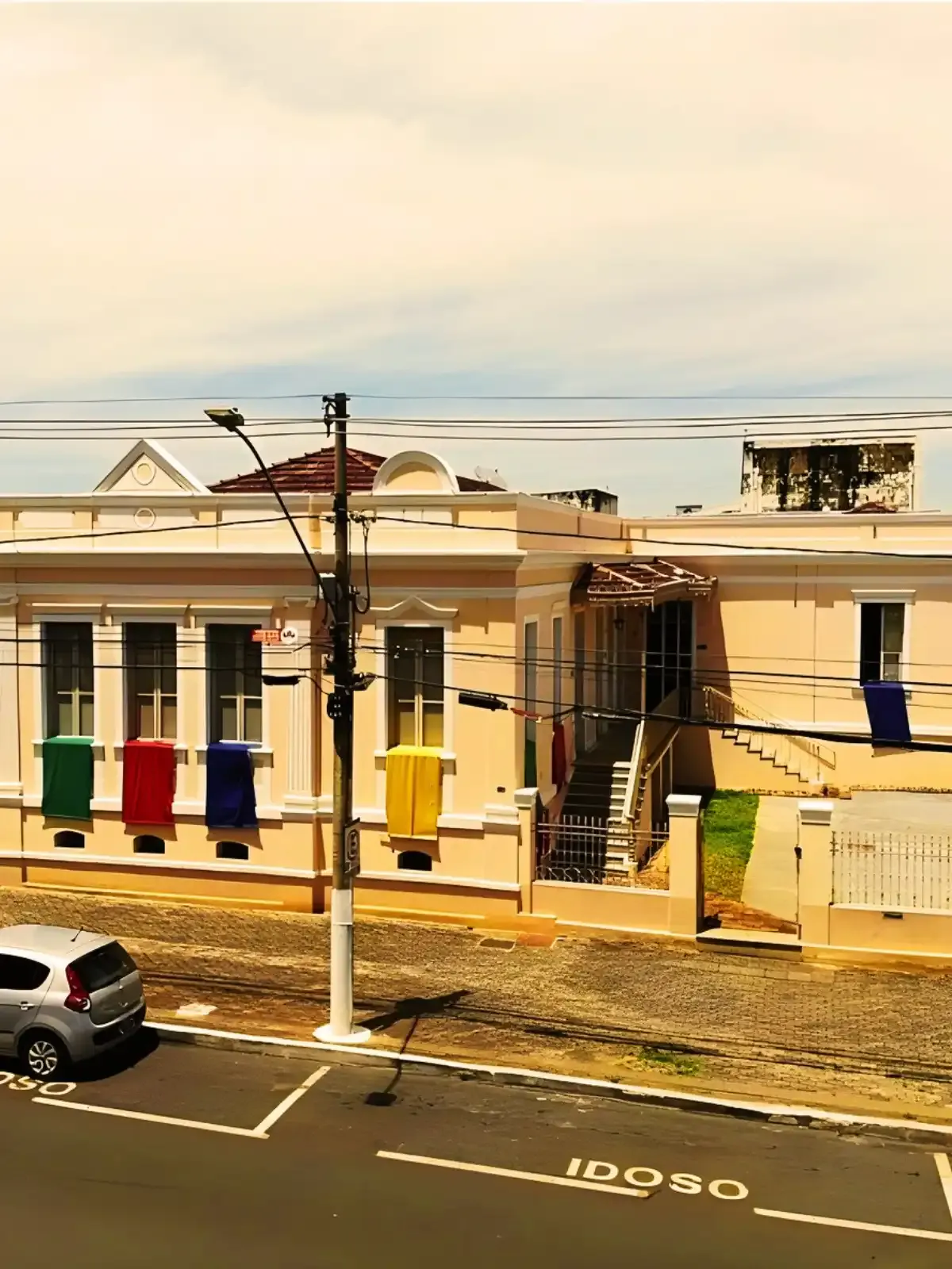 Imagem de fachada de uma casa colorida com decoração de panos de forma de bandeirinhas na cidade, com ruas movimentadas e uma lâmpada de rua.