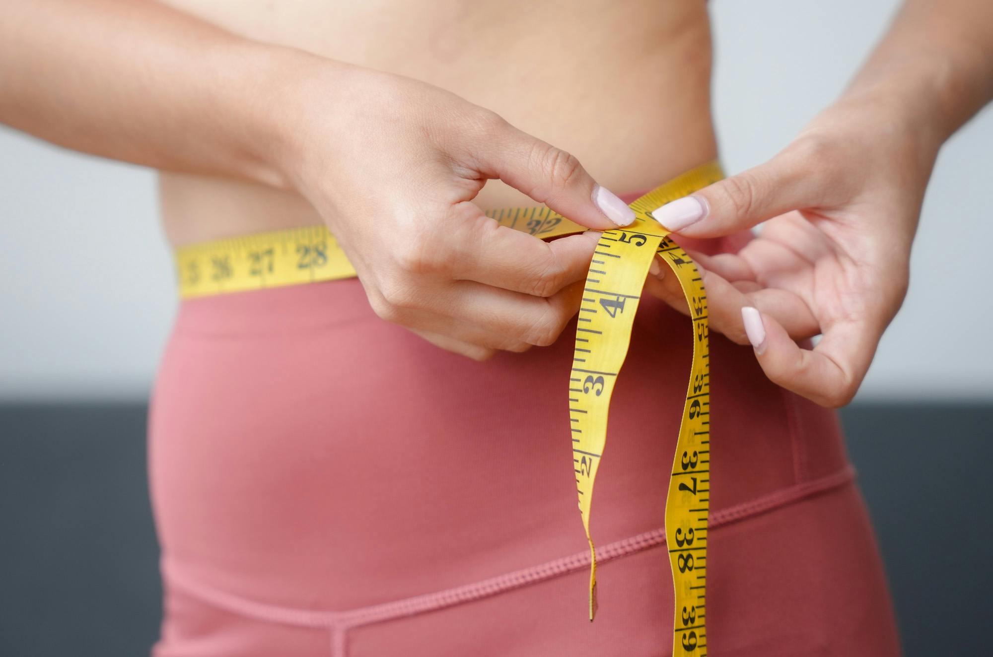 A woman measuring her waist with a tape measure to denote weight management