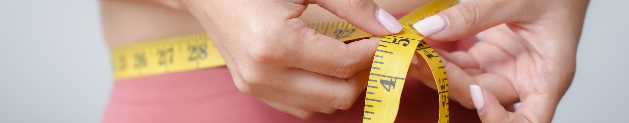 A woman measuring her waist with a tape measure to denote weight management