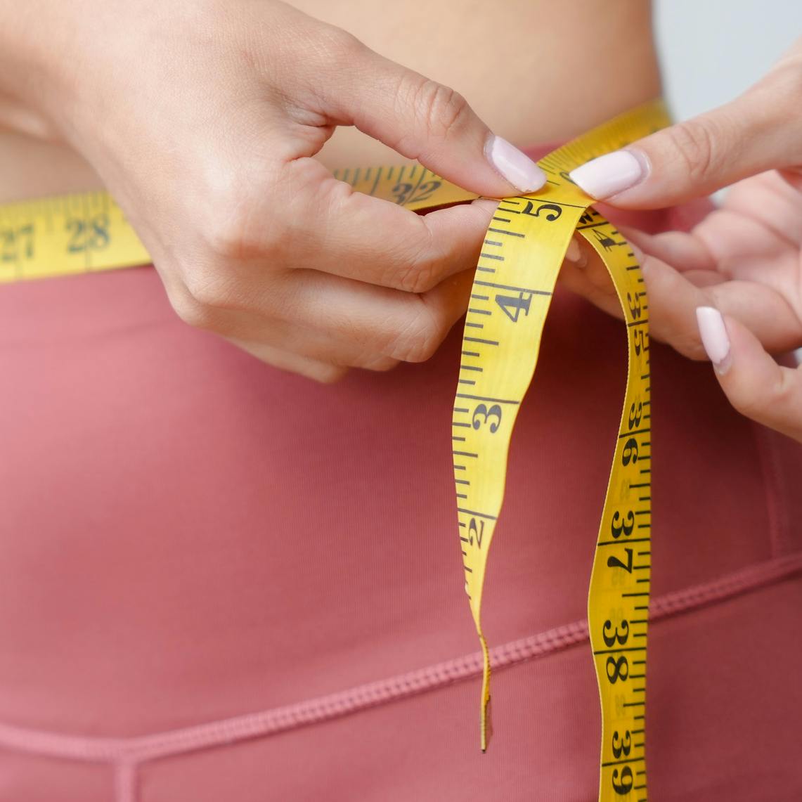 A woman measuring her waist with a tape measure to denote weight management