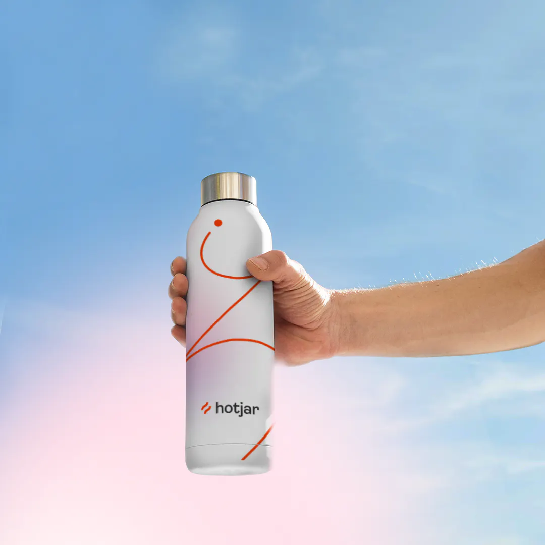 Hand holding up a white Hotjar water bottle with a red line design against a blue sky