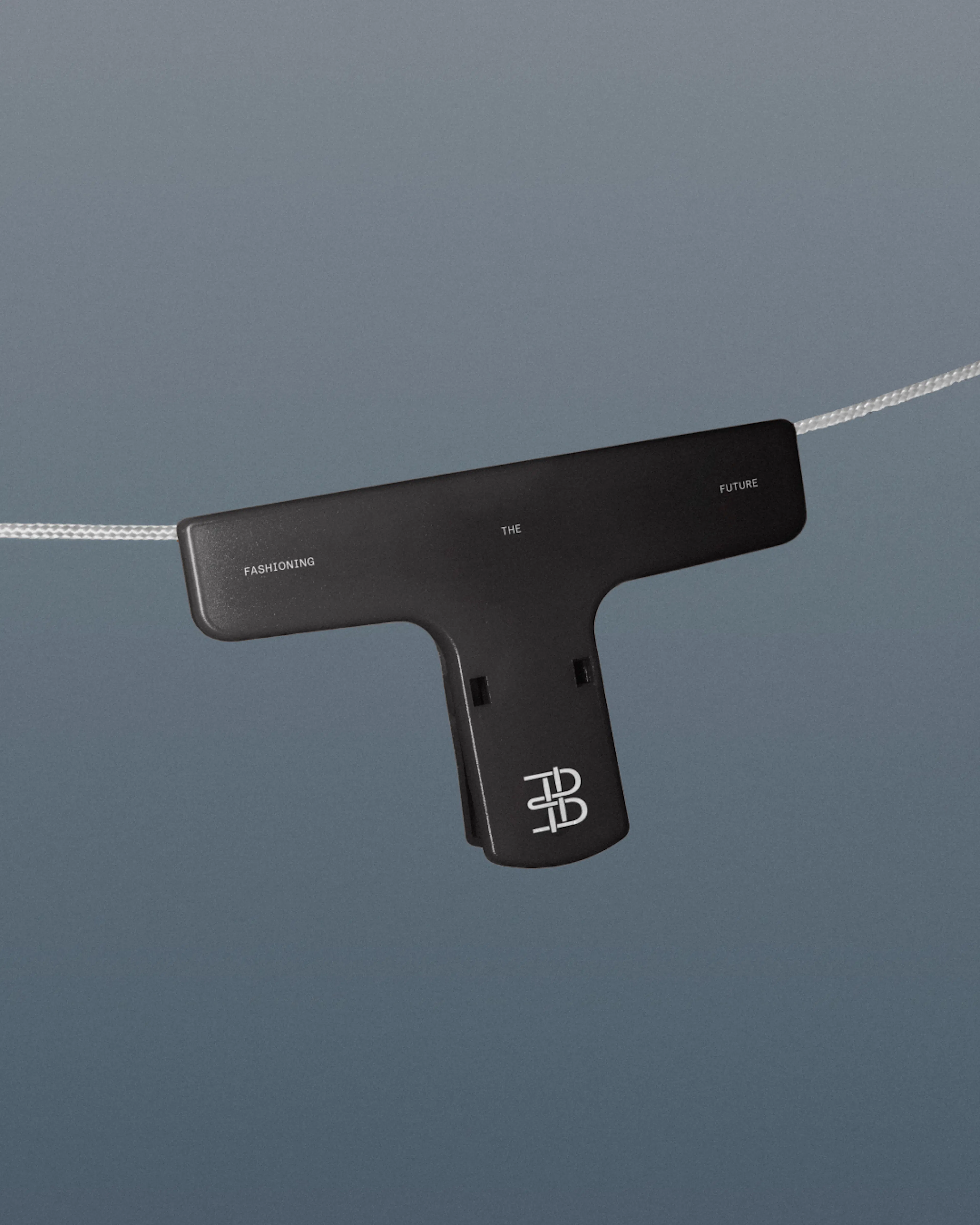 Black T-shaped clip with the Everbloom monogram hanging from a fine thread