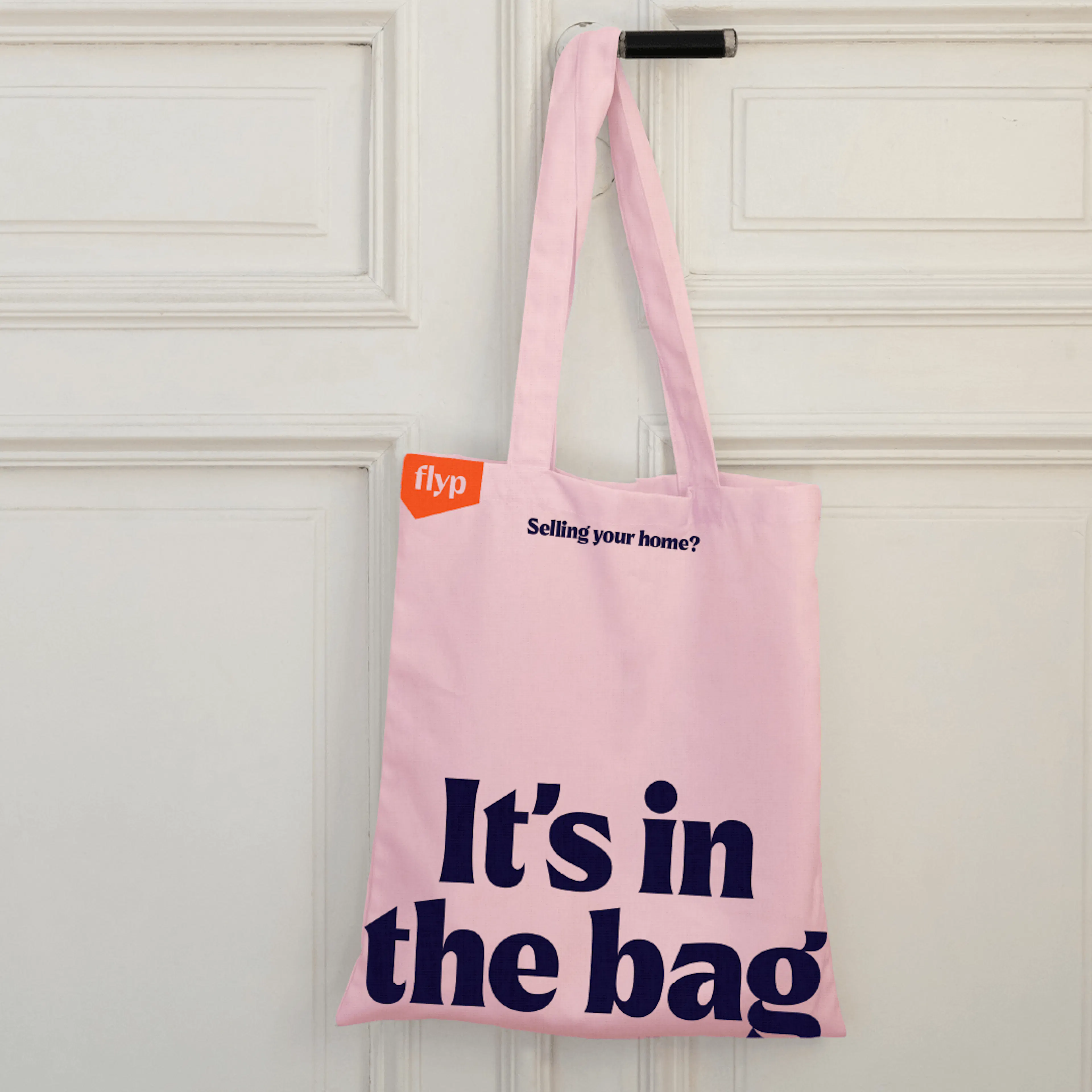 Pink flyp tote bag reading 'It's in the bag' hanging on a white door